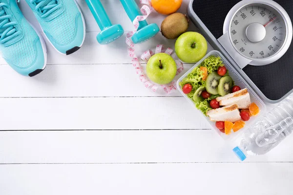 Healthy lifestyle, food and sport concept. Top view of athlete\'s equipment Weight Scale measuring tape blue dumbbell, sport water bottles, fruit and vegetables on white wooden background.