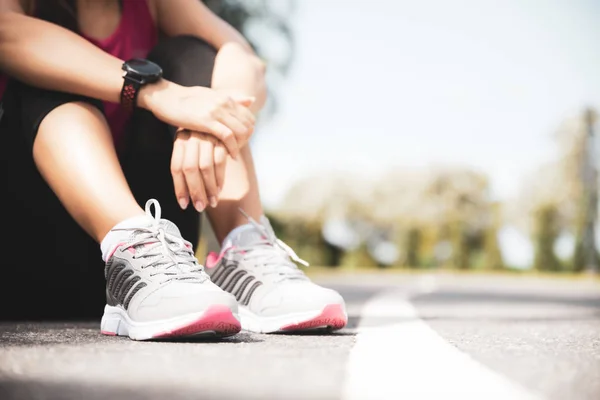 Modelo de fitness femenino sentado en la calle a lo largo de estanque en la ciudad. Mujer joven corredora descansando después de la sesión de entrenamiento en la mañana soleada. Concepto de Deportes y Recreación . — Foto de Stock