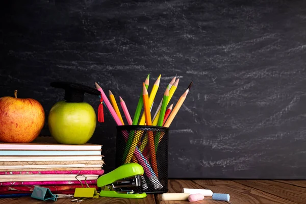Onderwijs of terug naar school concept. Kleurrijke schoolbenodigdheden met boeken, kleurpotloden, Calculator, pen Cutter clips en groene appel op schoolbord achtergrond. — Stockfoto