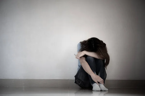 Mujer triste abrazar su rodilla y llorar. Mujer triste sentada sola en una habitación vacía . — Foto de Stock