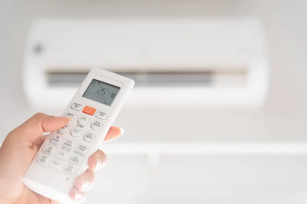 Mulher mão segurando controlador remoto dirigido sobre o ar condicionado dentro da sala e definido à temperatura ambiente, 25 graus celsius . — Fotografia de Stock