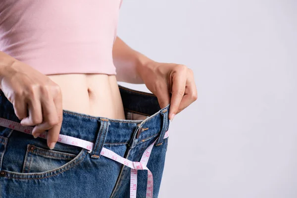 Feche a jovem magro medindo sua cintura fina com uma fita métrica. Cuidados de saúde e conceito de estilo de vida da dieta da mulher para reduzir a barriga e moldar o músculo do estômago saudável . — Fotografia de Stock