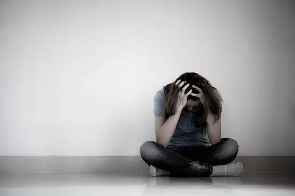 悲伤的女人抱着她的膝盖和哭泣。悲伤的女人独自坐在空荡荡的房间. — 图库照片