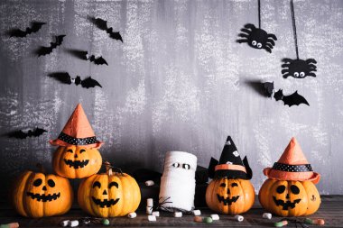 Gri tahta arka planda sopalı cadı şapkalı turuncu hayalet balkabakları. Cadılar Bayramı konsepti.