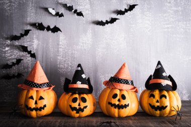 Gri tahta arka planda sopalı cadı şapkalı turuncu hayalet balkabakları. Cadılar Bayramı konsepti.