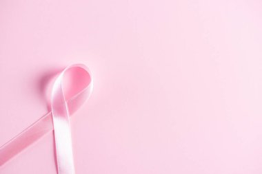 Göğüs kanseri farkındalığı kampanyasını desteklemek için pembe pastel kağıt üzerine pembe kurdele..
