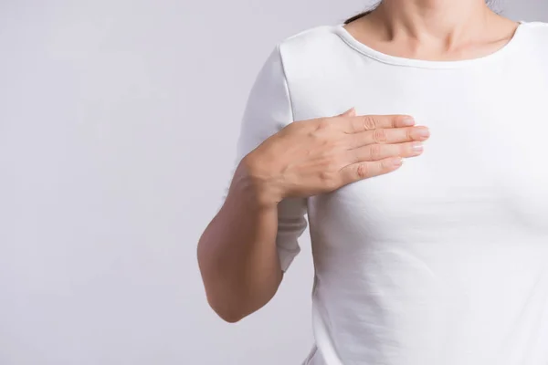 Mano de mujer revisando bultos en su pecho en busca de signos de cáncer de mama sobre fondo gris. Concepto sanitario. — Foto de Stock