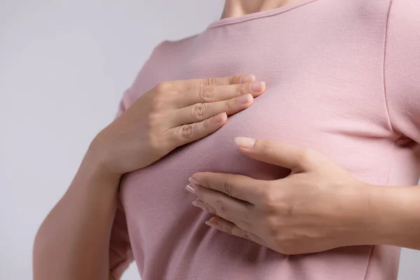 Mano de mujer revisando bultos en su pecho en busca de signos de cáncer de mama sobre fondo gris. Concepto sanitario. — Foto de Stock