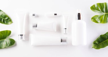 Kozmetik şişe kapları, yeşil bitkisel yapraklı cilt kremi. Doğal güzellik ve kaplıca konsepti, beyaz masa arka planında üstten görünüm.