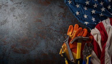 İşçi Bayramı konseptin kutlu olsun. Koyu taş zemin üzerinde farklı inşaat araçlarına sahip Amerikan bayrağı, metin için kopyalama alanı.