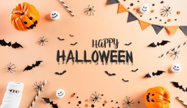 Cadılar Bayramı süslemeleri balkabağı, kağıt yarasalar ve pastel turuncu arka planda siyah örümcekten yapılır. Düz yatış, üst görünüm Mutlu Cadılar Bayramı metni.