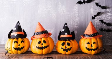 Gri tahta arka planda sopalı cadı şapkalı turuncu hayalet balkabakları. Cadılar Bayramı konsepti.