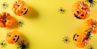 Cadılar Bayramı el sanatları, turuncu hayalet balkabağı ve pastel sarısı arka planda siyah örümcek. Düz konum, kopyalama alanı olan üst görünüm.