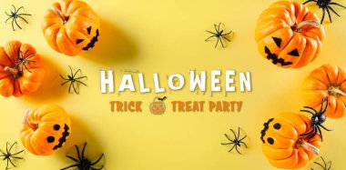 Cadılar Bayramı el sanatları, turuncu balkabağı, hayalet, yarasa ve sarı arka planda siyah örümcek. Düz yatış, Cadılar Bayramı metniyle üstten görünüm.