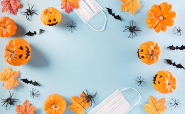 Cadılar Bayramı süslemeleri, pastel mavi arka planda balkabağı, kağıt yarasalar ve cerrahi maske. Covid-19 salgını sırasındaki Cadılar Bayramı kutlamalarının üst görüntüsü..