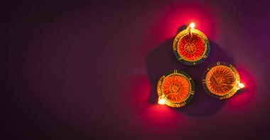 Mutlu Diwaliler - Dipavali sırasında Clay Diya lambaları yandı, Hindu ışık festivali kutlaması. Mor arka planda renkli geleneksel gaz lambası diya
