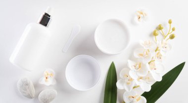 Kozmetik şişe kapları, yeşil bitkisel yapraklı cilt kremi. Doğal güzellik ve kaplıca konsepti, beyaz masa arka planında üstten görünüm.