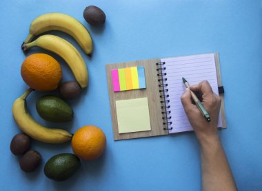 mavi bir arka plan üzerinde yaylar notlar Etiketler renkli el üstünde defter kalem kolu meyve portakal muz avokado kivi yazmak