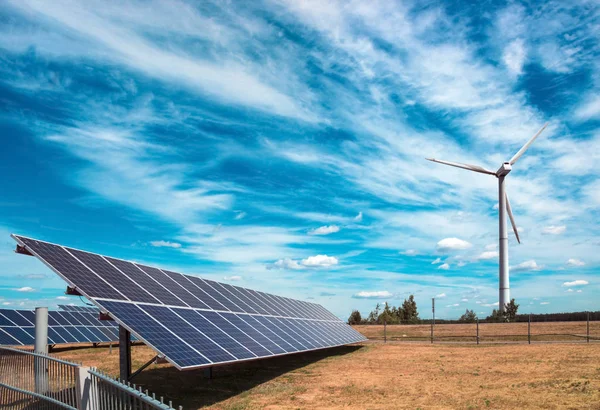 Generador eólico de electricidad a partir de tres palas y baterías de paneles solares de fotocélulas sobre un fondo de nubes y cielo azul —  Fotos de Stock