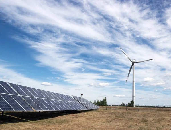 Generador eólico de electricidad a partir de tres palas y baterías de paneles solares de fotocélulas sobre un fondo de nubes y cielo —  Fotos de Stock