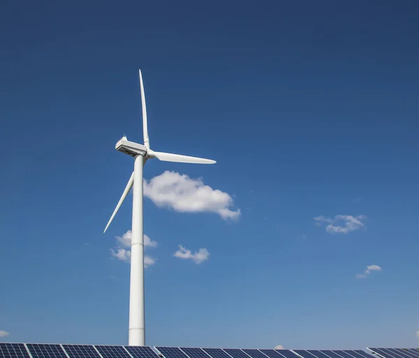 Generador eólico de electricidad a partir de tres hojas y paneles solares de una batería de fotocélulas sobre un fondo de nubes y una hierba verde cielo azul —  Fotos de Stock