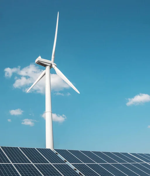 Generador eólico de electricidad a partir de tres hojas y paneles solares de una batería de fotocélulas sobre un fondo de nubes y un cielo azul —  Fotos de Stock