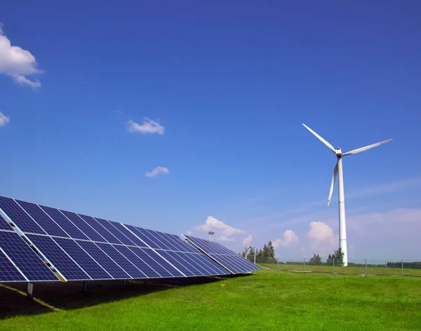 Generador eólico de electricidad a partir de tres hojas y paneles solares de una batería de fotocélulas sobre un fondo de nubes y una hierba verde cielo azul —  Fotos de Stock