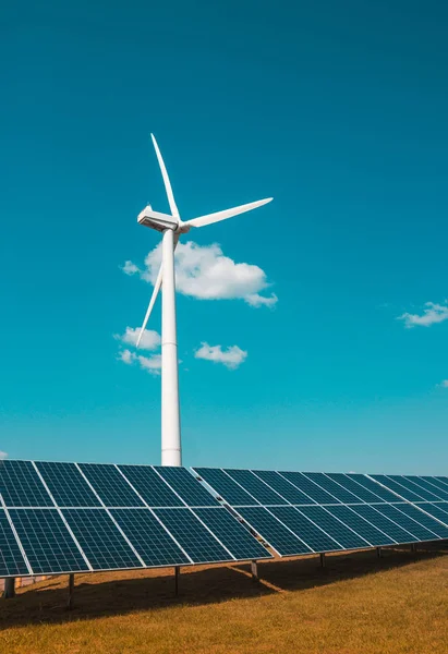 Generador eólico de electricidad a partir de tres hojas y paneles solares de una batería de fotocélulas sobre un fondo de nubes y una hierba naranja cielo azul —  Fotos de Stock