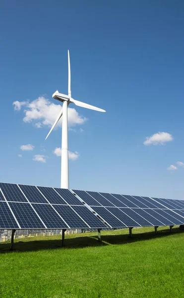 Generador eólico de electricidad a partir de tres hojas y paneles solares de una batería de fotocélulas sobre un fondo de nubes y una hierba verde cielo azul —  Fotos de Stock