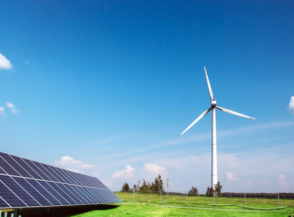 Generador eólico de electricidad a partir de tres hojas y paneles solares de una batería de fotocélulas sobre un fondo de nubes y una hierba verde cielo azul —  Fotos de Stock