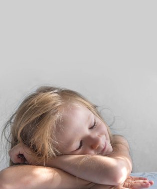 gri bir arka plan üzerinde uyuyan bir gülümseyen kız güneş sabah ışınları içinde yatıyor.