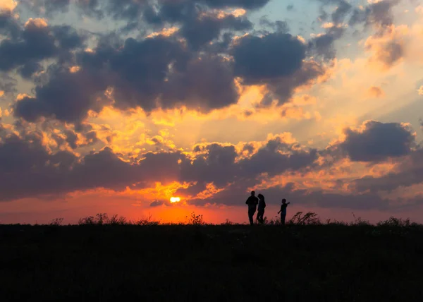 Atardecer amanecer rayos de sol sobre campo cielo campo familia caminando cerca del sol en el horizonte silueta — Foto de Stock