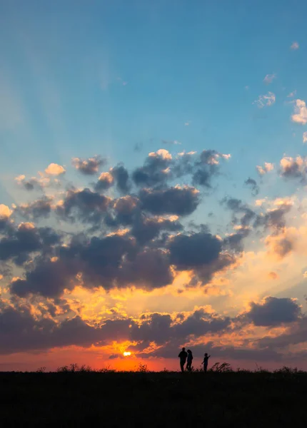Atardecer amanecer rayos de sol sobre campo cielo campo familia caminando cerca del sol en el horizonte silueta — Foto de Stock