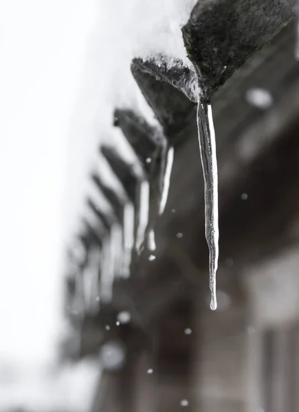 Icicles pendurar e neve cai no telhado de uma casa de madeira — Fotografia de Stock