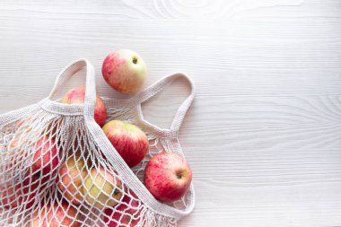 Ahşap bir arka planda yeniden kullanılabilir beyaz bir çevre dostu çanta ve meyve elmaları var.