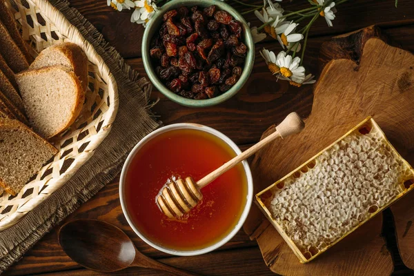 Honigtopf und Löffel am rustikalen Tisch mit Brot, Rosinen und Honigwaben, von oben — Stockfoto