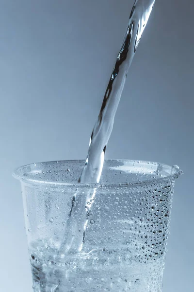 순수한 신선한 물 유리 또는 플라스틱 컵에서 가까이 건강 음료를 쏟아 — 스톡 사진