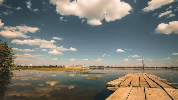Panorama della Centrale Elettrica e nuvole riflesse nel fiume con molo in legno in primo piano — Foto Stock