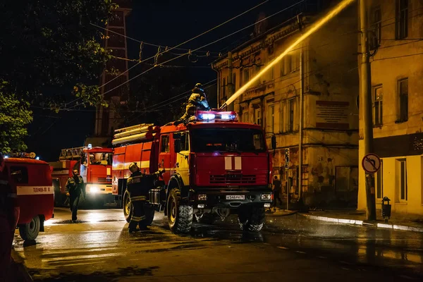 Рибінська, Росія-31 липня 2018: з пожежників вогонь шланг і пожежних машин або вантажівок борються вогонь у житловому будинку на ніч. Величезний диму, полум'я в горить будинок — стокове фото