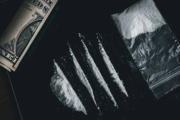 Kokain-Pulverlinien, gerollte Banknoten und Drogen in Plastiktasche auf schwarzer Glasoberfläche, Ansicht von oben. Drogenabhängiges Konzept — Stockfoto