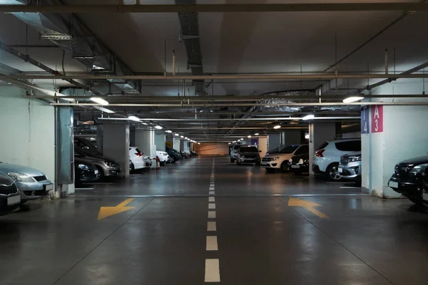 Illuminated underground car parking interior under modern mall with lots of vehicles and arrows on floor — Stock Photo, Image