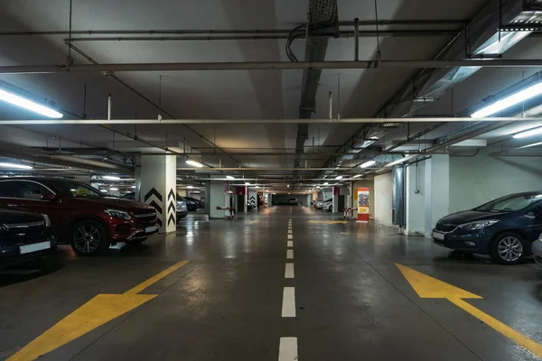 Parking souterrain éclairé intérieur sous le centre commercial moderne avec beaucoup de véhicules et des flèches sur le sol — Photo