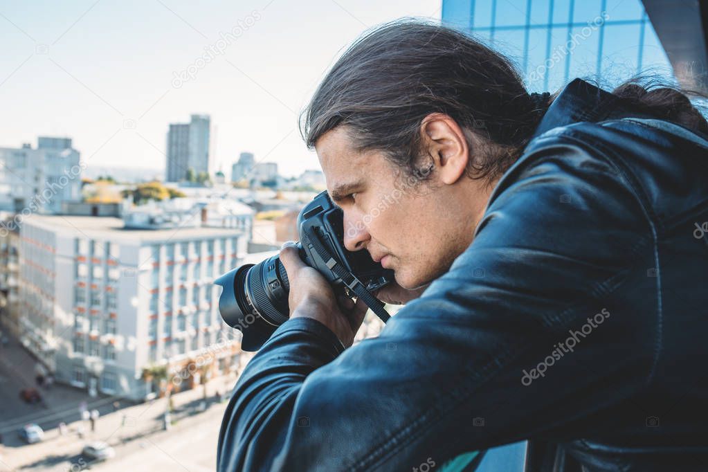 Investigator or private detective or reporter or paparazzi taking photo from balcony of building with professional camera