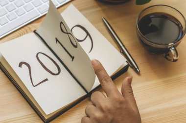 Yeni yıl 2019 önümüzdeki kavramdır. El ahşap masa üzerinde Not Defteri sayfası döndürür. 2018 dönüyor, 2019 açma