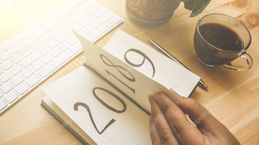 New Year 2019 is coming concept. Female hand flips notepad sheet on wooden table. 2018 is turning, 2019 is opening