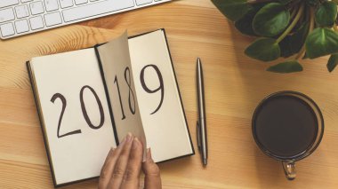Yeni yıl 2019 önümüzdeki kavramdır. El ahşap masa üzerinde Not Defteri sayfası döndürür. 2018 dönüyor, 2019 açma