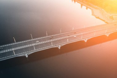 Drone ile asfalt yolda veya otobanda günbatımı ışık, kentsel ulaşım şehir araba trafik ile büyük nehir üzerinde beton köprü hava veya üst görünümden