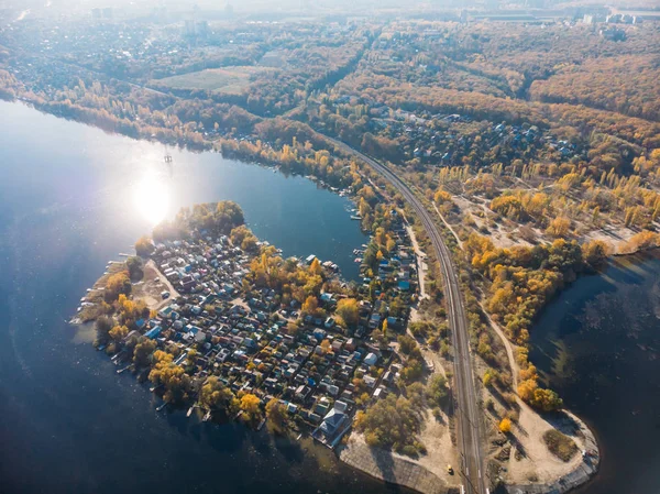 Suburban village with many small houses near railroad and big blue river, aerial view