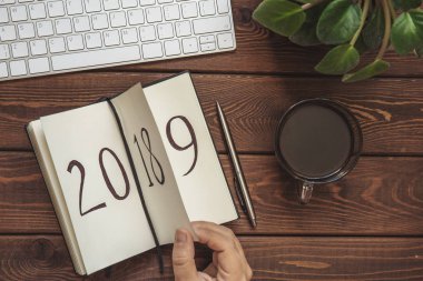 Yeni yıl 2019 önümüzdeki kavramdır. El ahşap masa üzerinde Not Defteri sayfası döndürür. 2018 çeviriyor, 2019 açıyor, ana sayfa görünümü