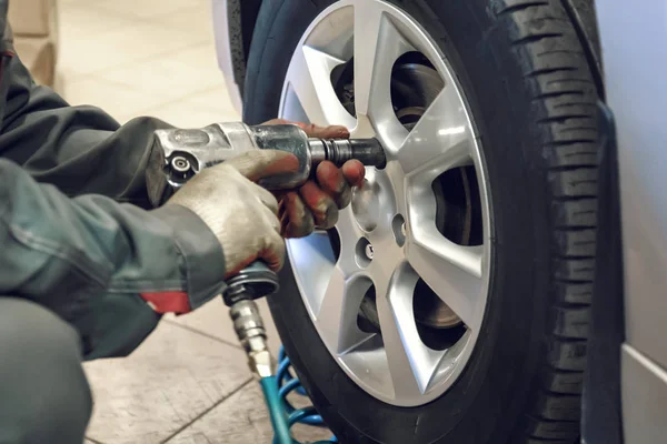 Substituindo pneus de verão para o inverno usando a ferramenta de chave pneumática pelo trabalhador mecânico depois de equilibrar as rodas na oficina de garagem de serviço de carro — Fotografia de Stock